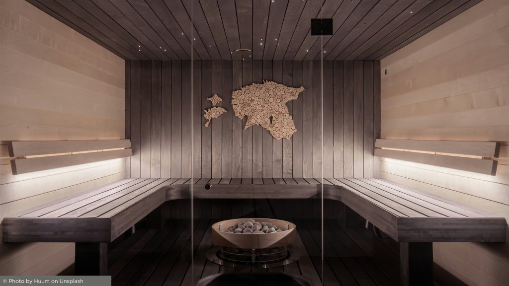 Sauna moderna com bancos de madeira, um mapa de toras da Estônia na parede, forno central de pedras, iluminação suave e painéis de vidro elegantes para um ambiente sereno